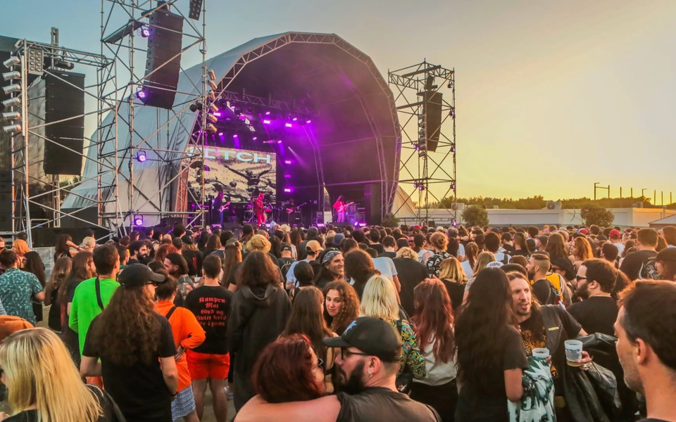 Crowd enjoying a heavy metal festival in Portugal at sunset with purple stage lights and live band performance.