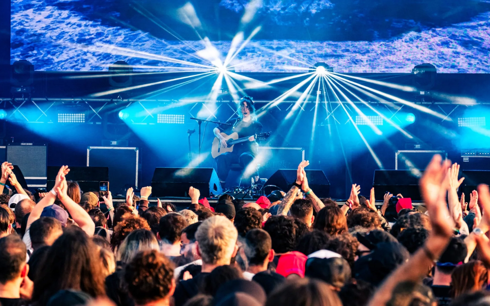 Acoustic guitarist performing live at SonicBlast Festival in Portugal with crowd cheering and bright stage lights.