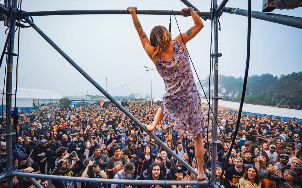 Performer climbing a stage structure during SonicBlast Festival in Portugal, with a large crowd cheering below.