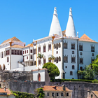 National Palace of Sintra with iconic twin chimneys, surrounded by greenery under a clear blue sky.