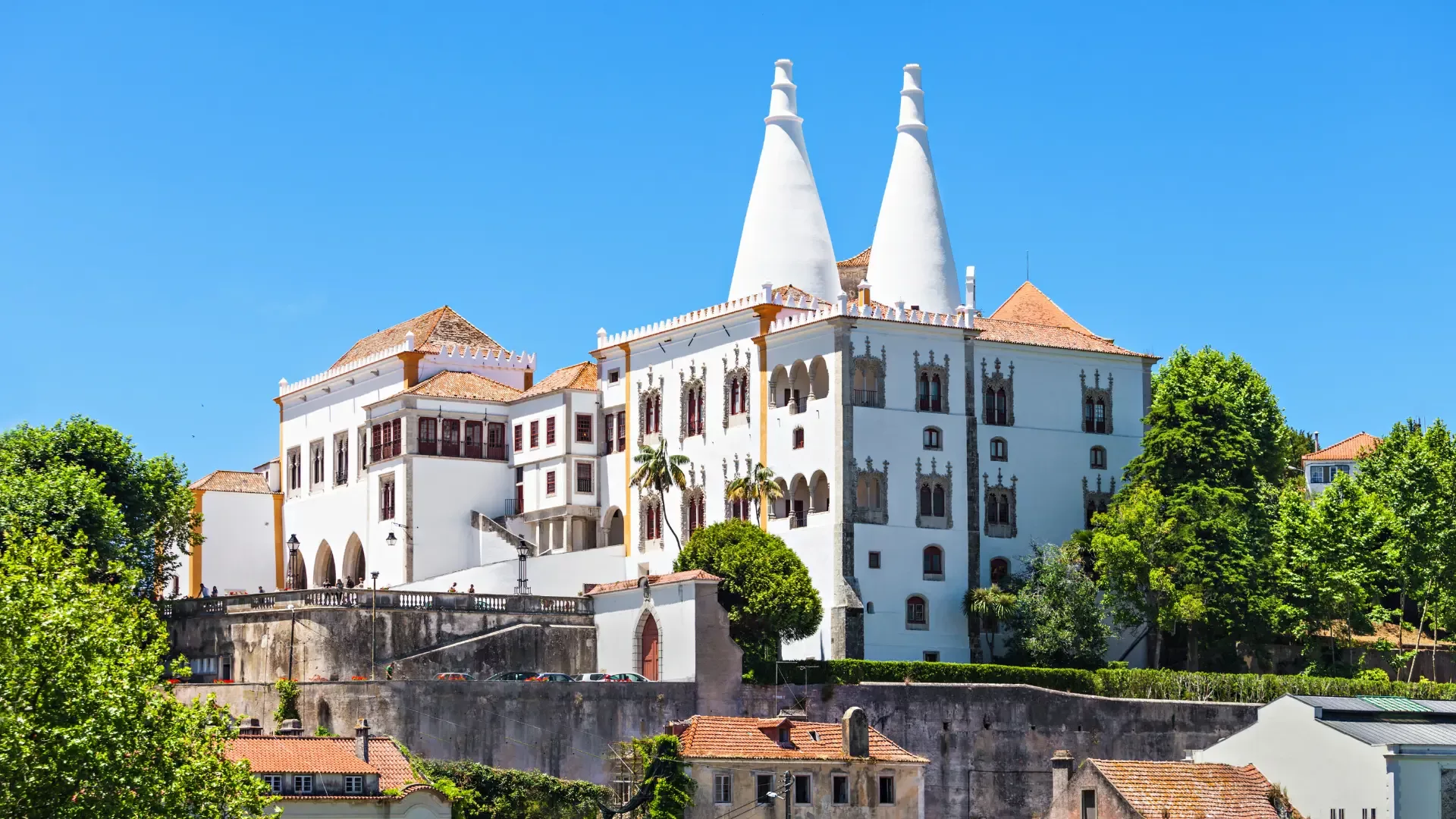 National Palace of Sintra with iconic twin chimneys, surrounded by greenery under a clear blue sky.