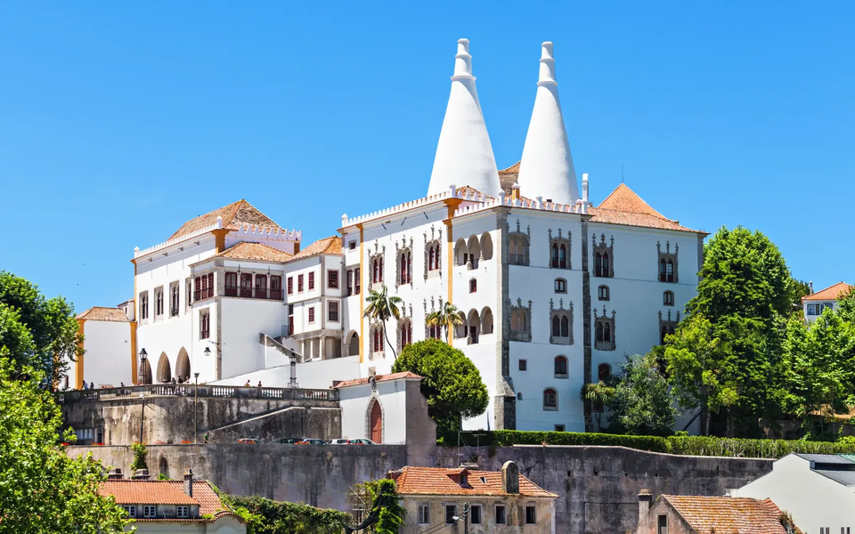 National Palace of Sintra with iconic twin chimneys, surrounded by greenery under a clear blue sky.