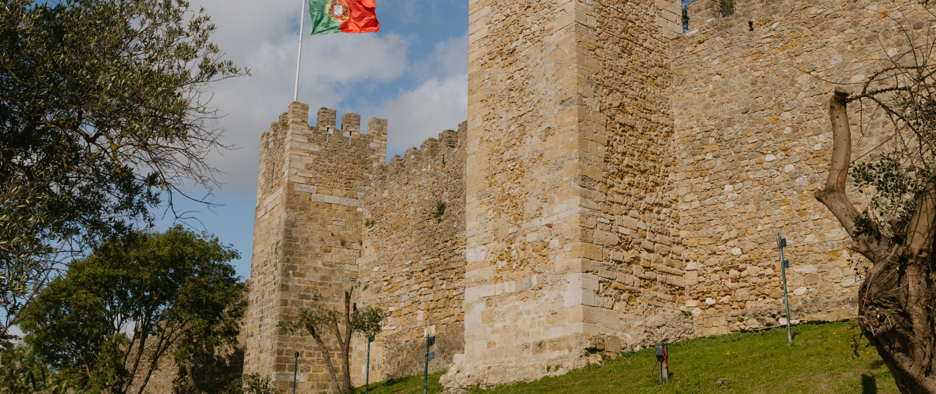 View of the historic São Jorge Castle walls with the Portuguese flag flying on a sunny day in Lisbon
