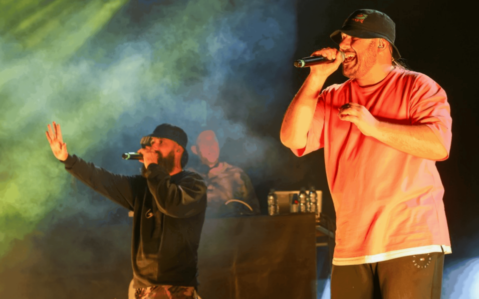 Live performance of two hip hop artists at the Throwback 00s Hip Hop & RnB event in Lisbon. They are on stage rapping with microphones, surrounded by atmospheric lighting and DJ setup in the background.