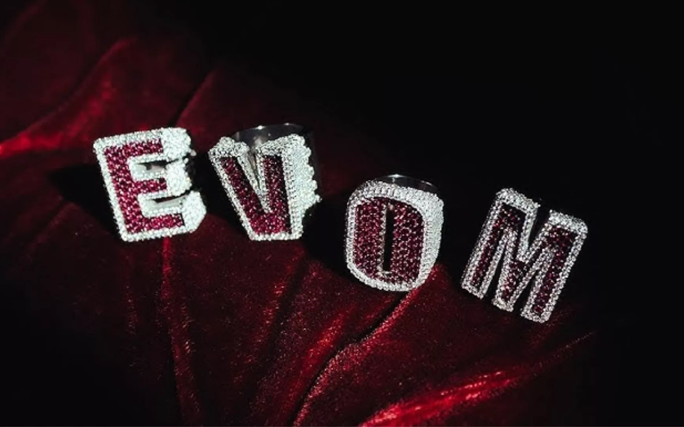 Close-up of diamond-studded rings spelling EVOM on red velvet fabric