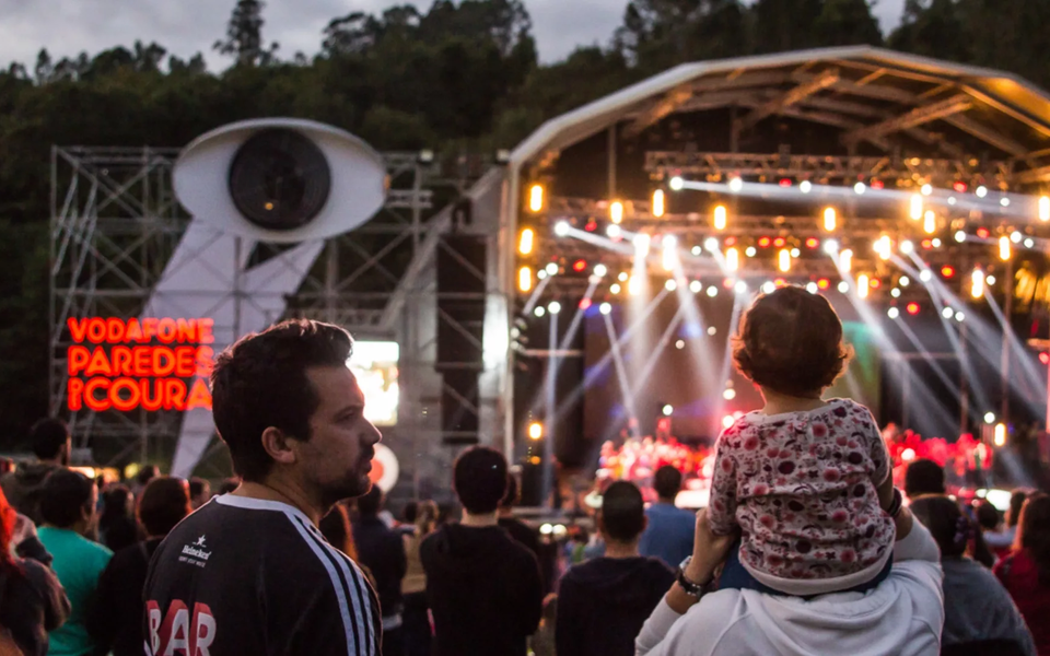 Audience enjoying a concert at Vodafone Paredes de Coura festival in Portugal, with stage lights and a family watching the show.
