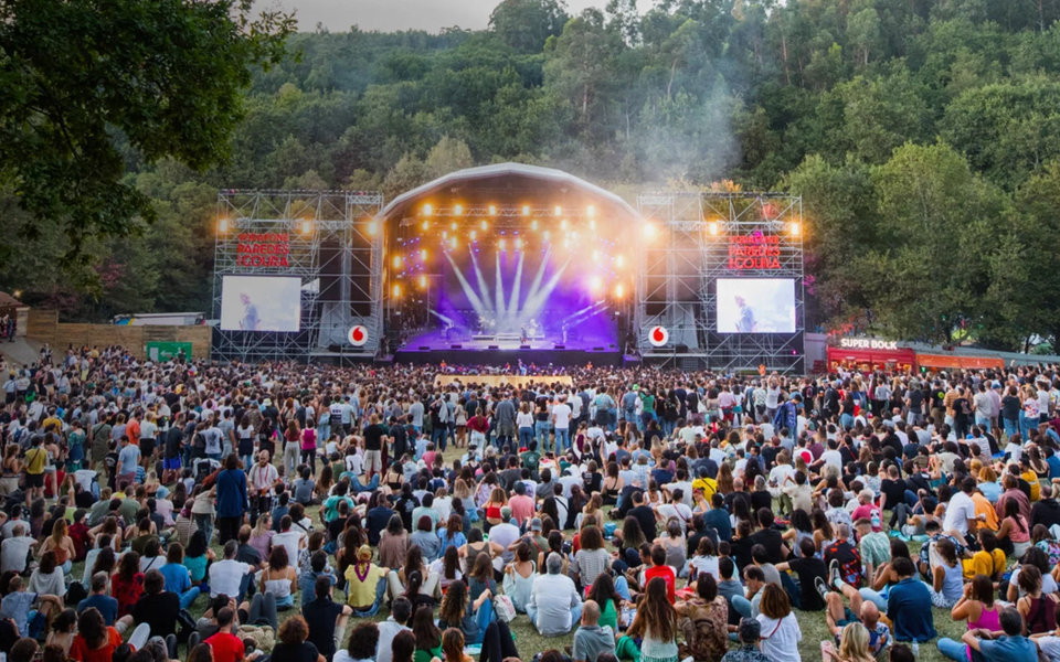 Full crowd gathered at Vodafone Paredes de Coura festival main stage in Portugal with bright yellow lights and forest backdrop.