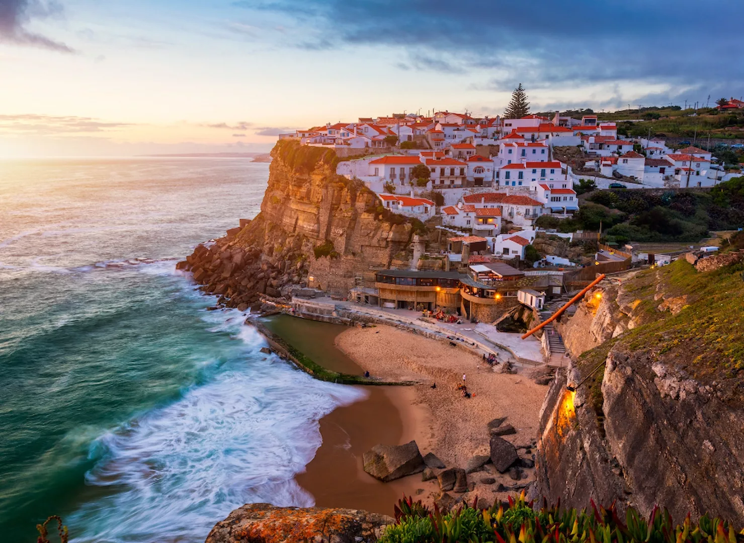 View of Azenhas do Mar village in Portugal at sunset, with its natural ocean pool and houses perched on the cliff.