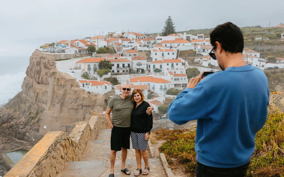 Elderly couple posing for a photo in Azenhas do Mar, a stunning seaside village perched on the cliffs of Portugal’s Atlantic coast.