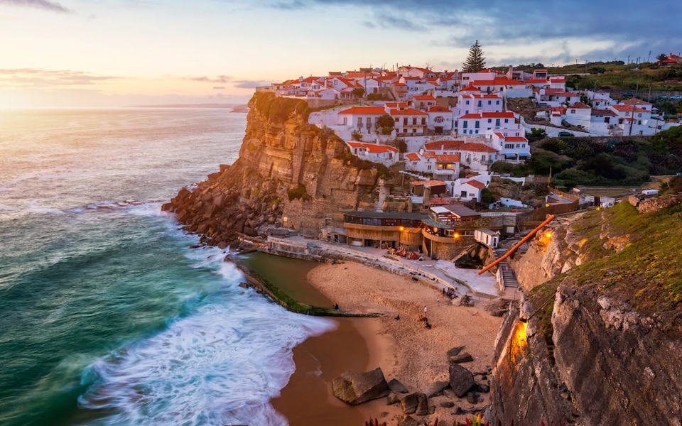 View of Azenhas do Mar village in Portugal at sunset, with its natural ocean pool and houses perched on the cliff.