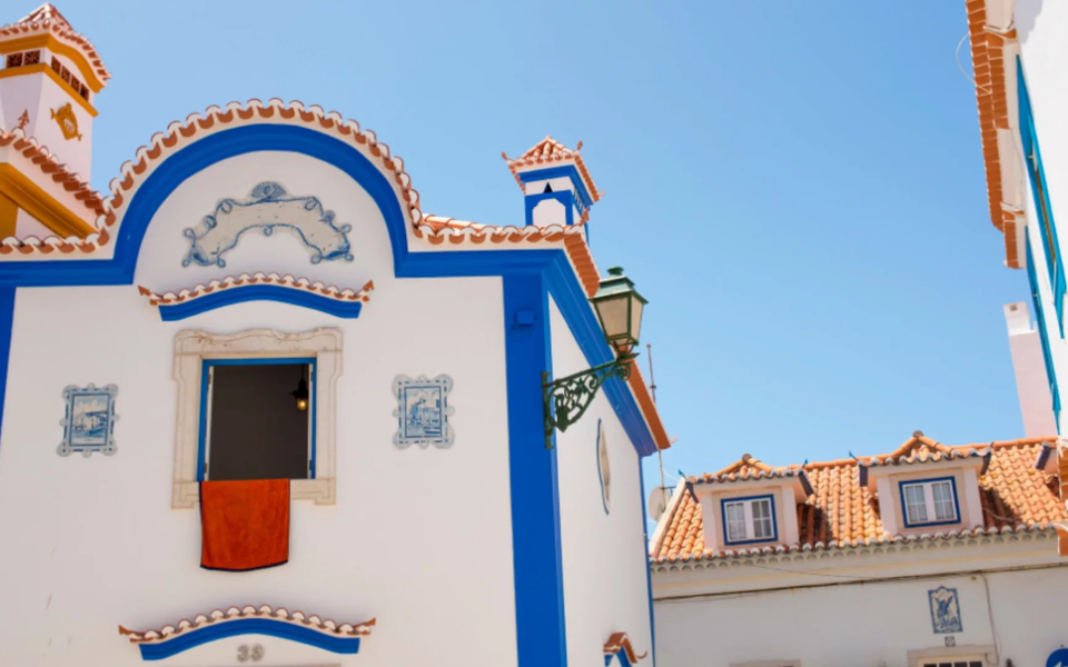 Traditional Portuguese houses in Ericeira with colorful blue trims, ceramic tiles and terracotta roofs under a bright summer sky.