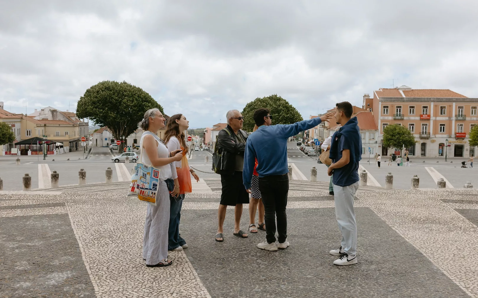 Tour guide leading a group of tourists in front of the Mafra National Palace, a monumental baroque building in Portugal.