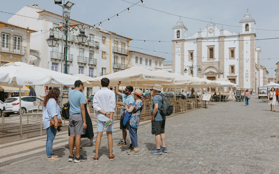 Tourists stand in Giraldo Square, Évora, engaging with a guide as they explore the lively plaza filled with history.
