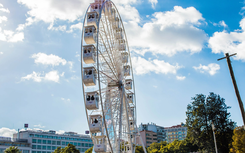 Large white Ferris wheel at Wonderland Lisboa during daytime with blue sky and city buildings in the background