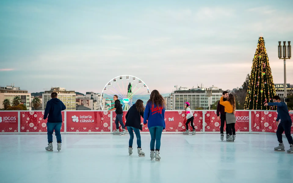 Children and adults ice skating at Wonderland Lisboa with the Ferris wheel and Christmas tree in the background
